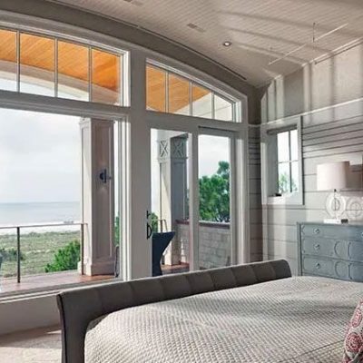 Interior view of a bedroom with a curved wall of windows and an open patio door leading to a beach view