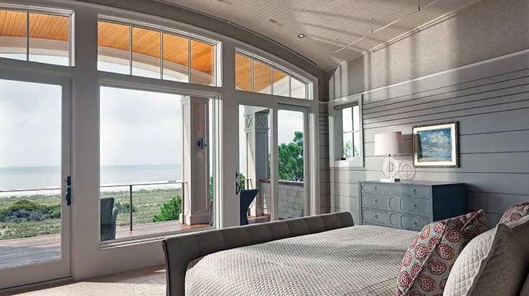 Interior view of a bedroom with a curved wall of windows and an open patio door leading to a beach view